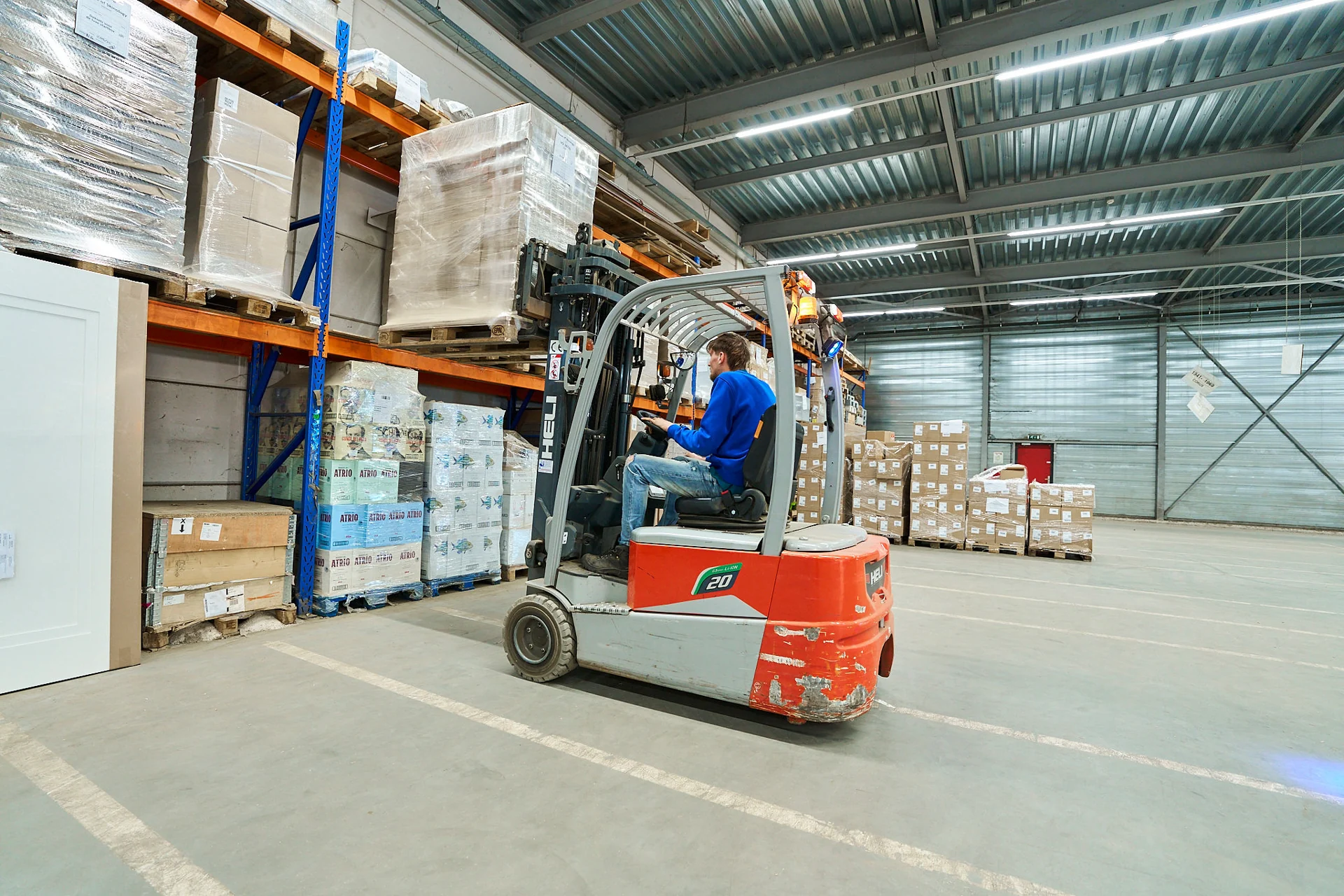 Medewerker op een heftruck naast stellingen met opgeslagen goederen