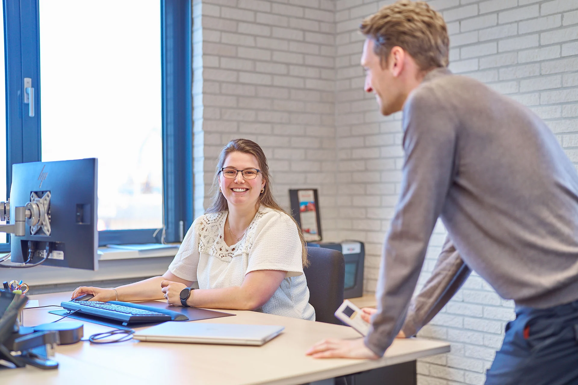 Twee collega’s overleggen bij een bureau op het kantoor van Brakenhoff