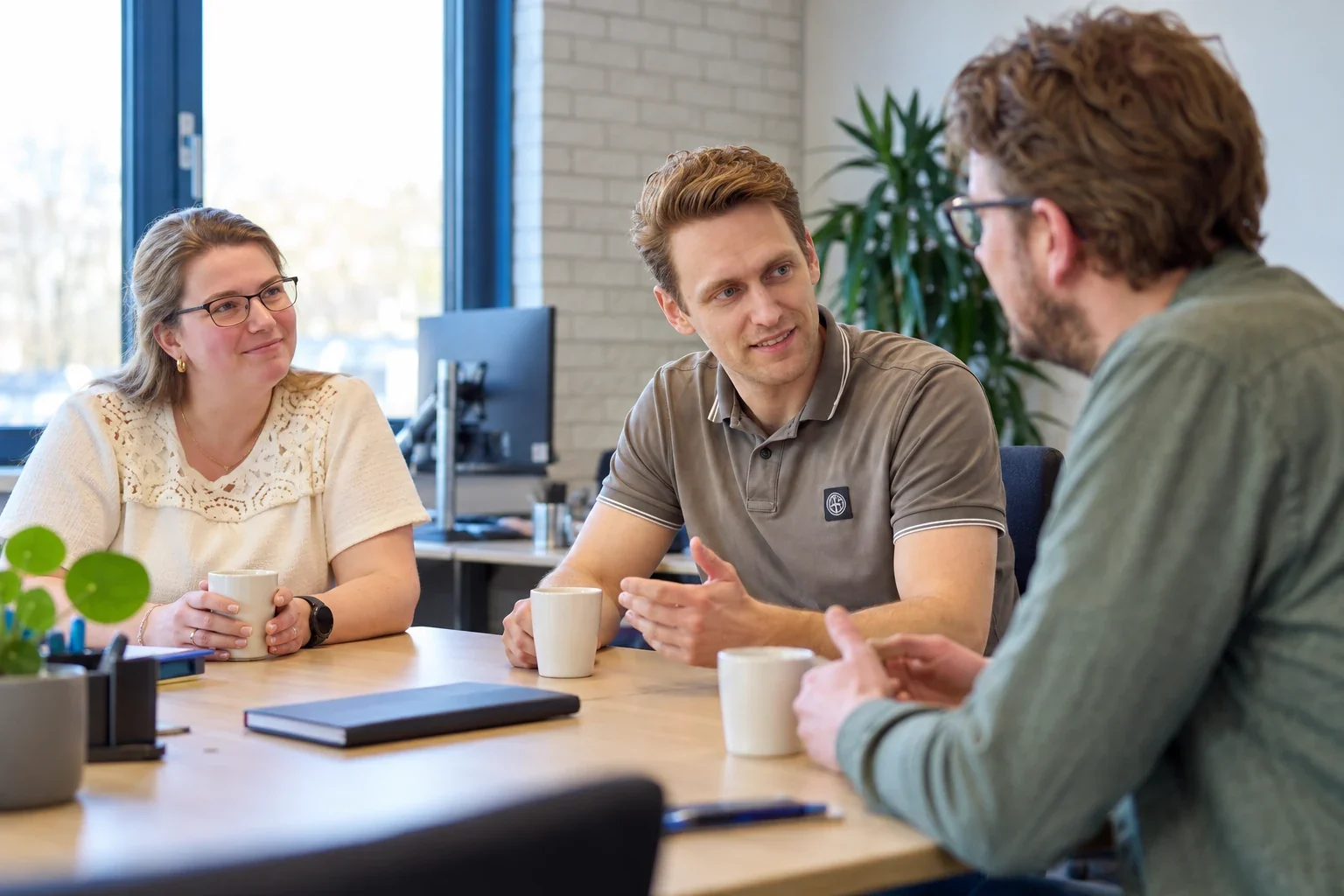 Drie mensen voeren een kennismakingsgesprek aan een tafel op kantoor